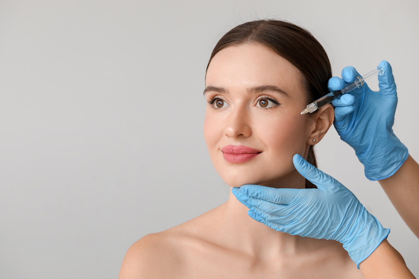 Young Woman Receiving Filler Injection against Grey Background